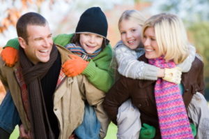 Parents outdoors piggybacking two young children and smiling